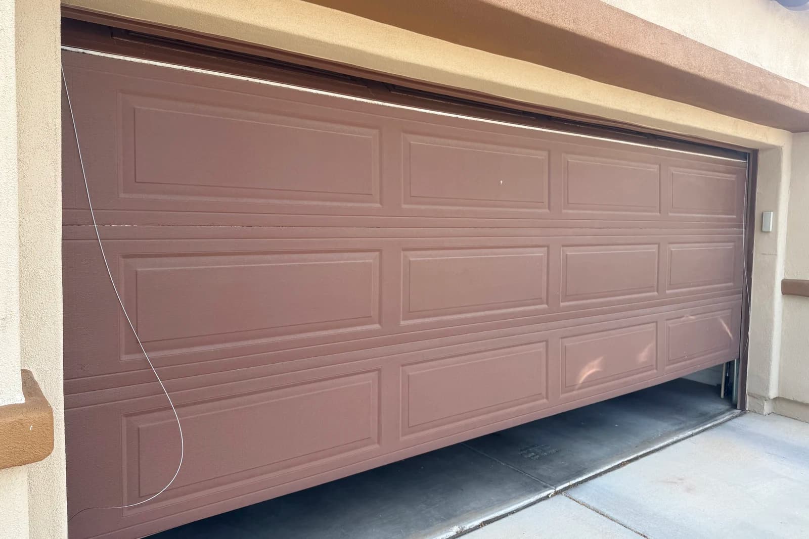 A Phoenix garage door hanging off-track with a loose cable after a broken garage door spring