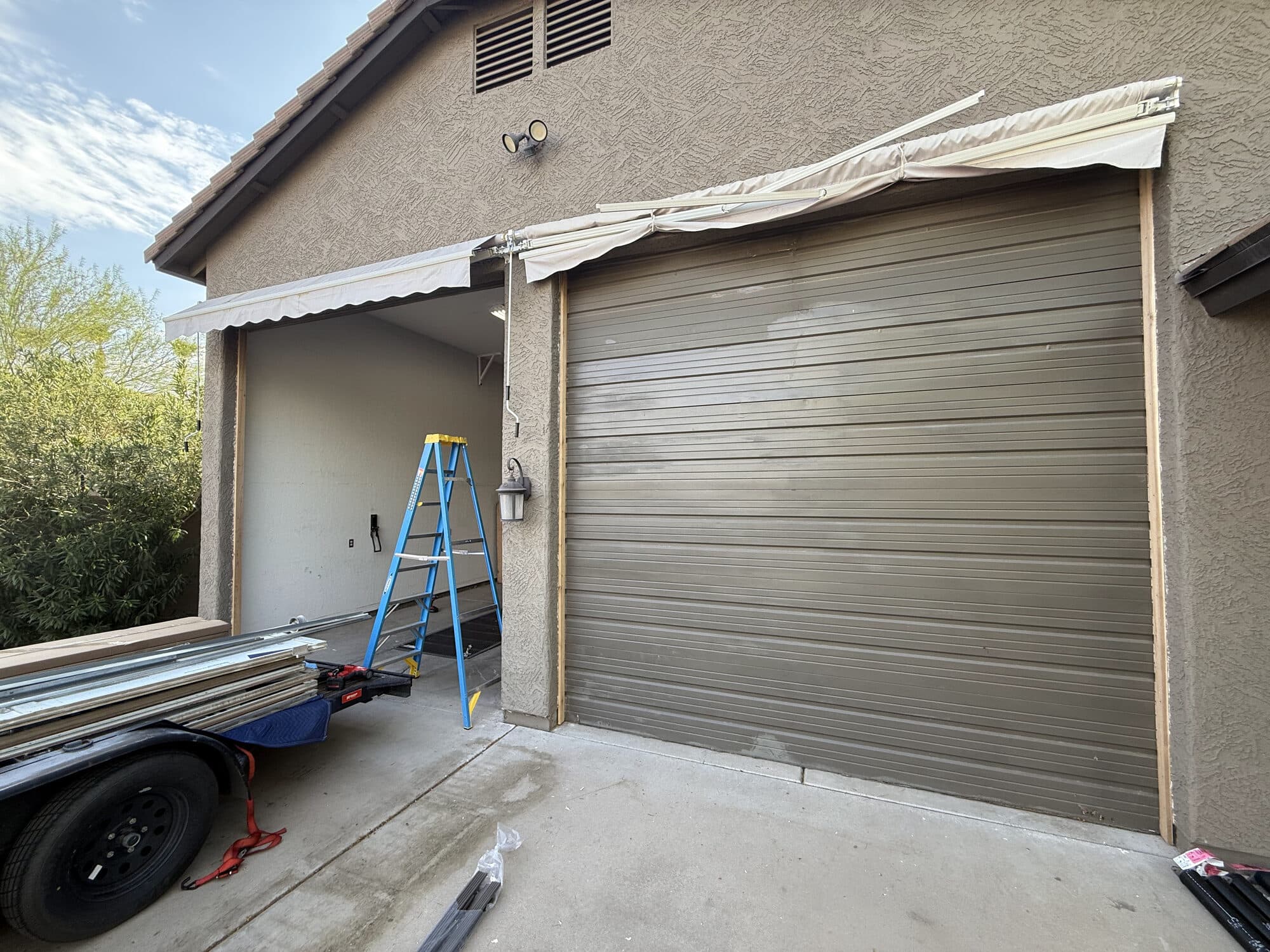 Old dingy, faded flat-panel garage door before replacement, with one bay already stripped, on a Glendale, AZ home
