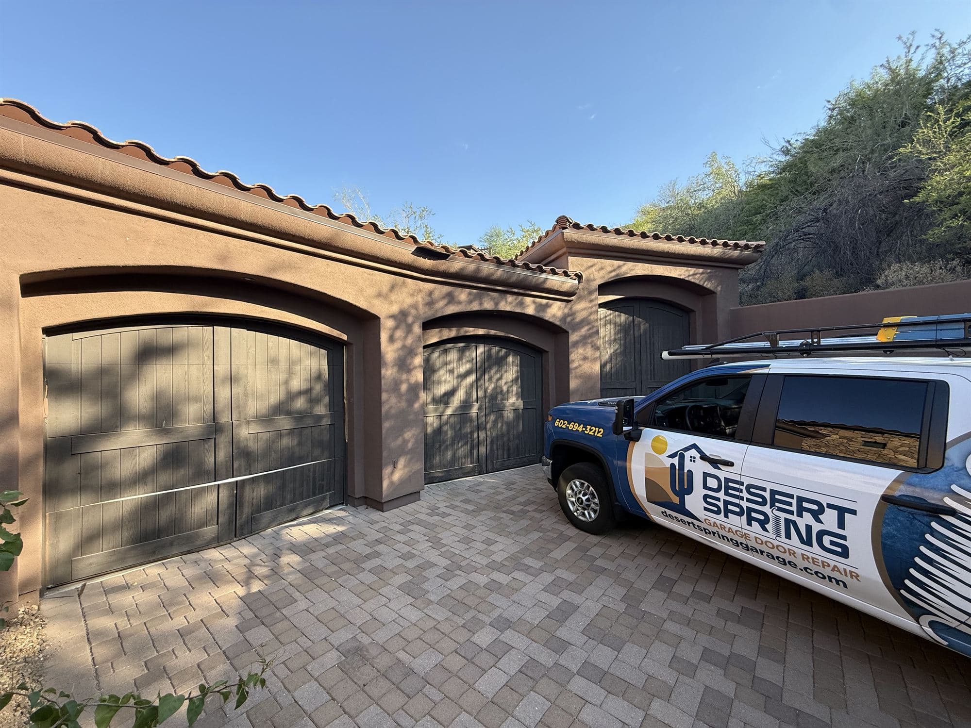 Three old weathered wooden garage doors before replacement, with the Desert Spring truck and new Clopay doors on site in Fountain Hills, AZ