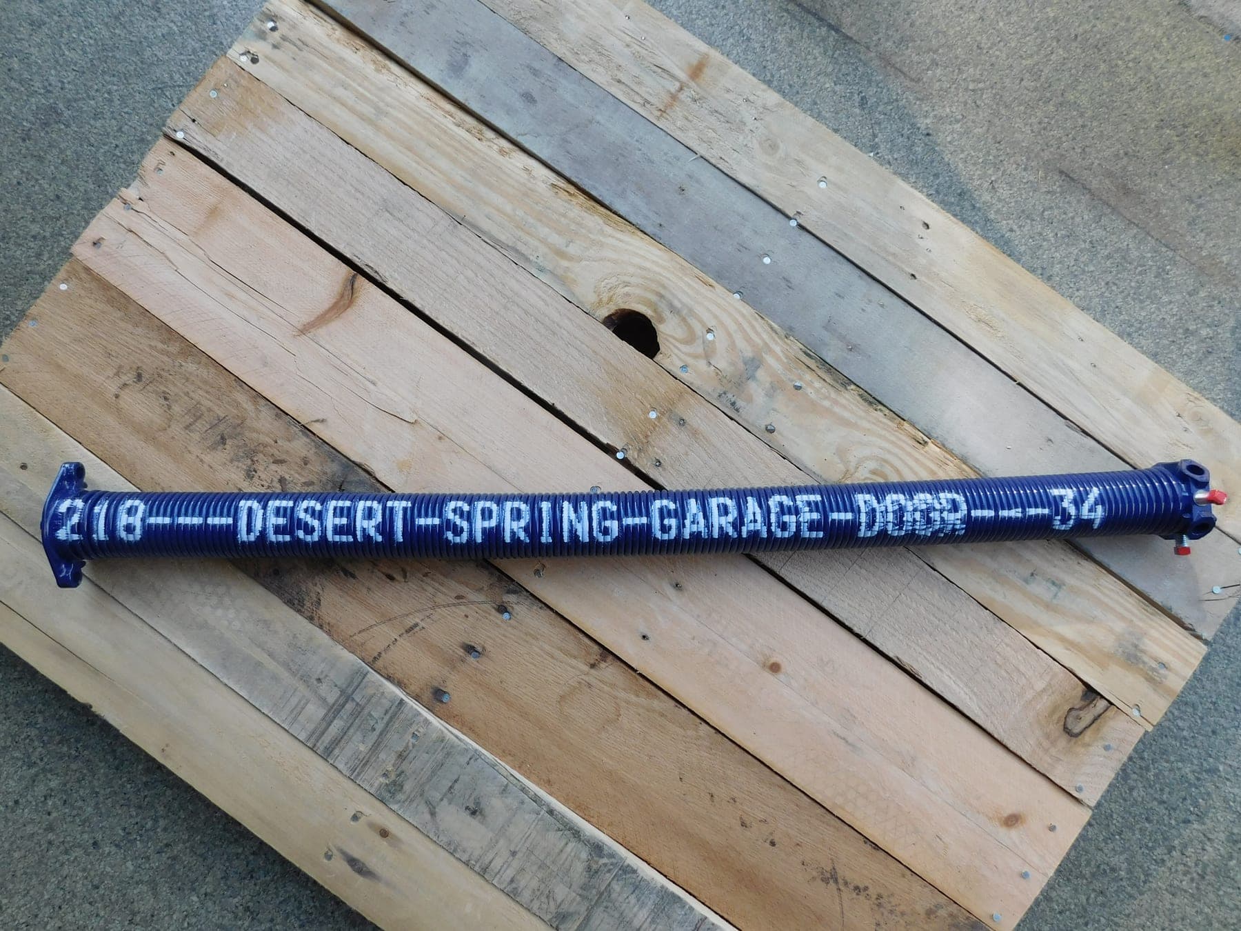 A single custom cobalt Desert Spring Performance Spring on rustic wood, stenciled DESERT-SPRING-GARAGE-DOOR with its exact size