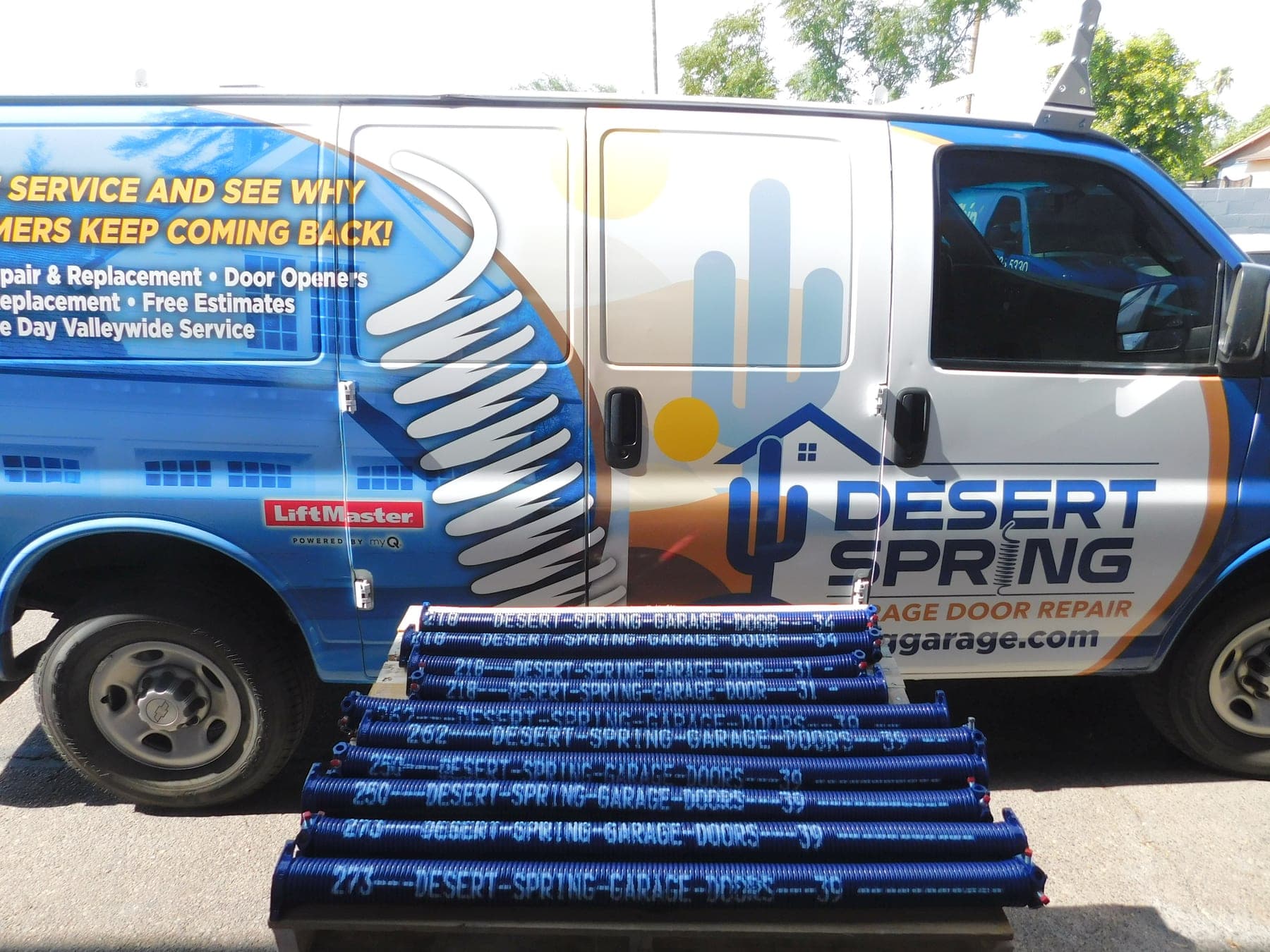 A batch of custom cobalt Desert Spring Performance Springs staged in front of the branded Desert Spring Garage Door Repair service van